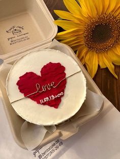 a cake in a box with the word love written on it next to a sunflower