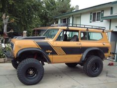 a yellow and black truck parked in front of a house with large tires on it