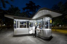 a man standing in front of a white bus stop at night with its lights on