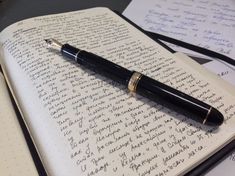 a pen sitting on top of an open notebook with writing in cursive ink