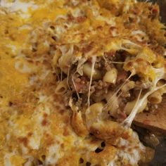 a casserole dish with meat and cheese being stirred by a wooden spoon