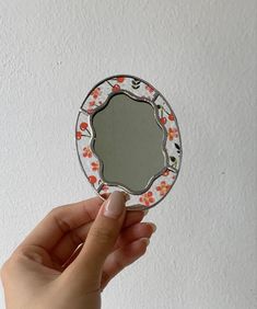 a hand holding a small mirror in front of a white wall with flowers on it