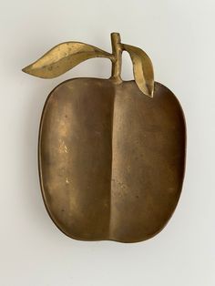 an apple shaped metal object hanging on the wall with a leaf attached to it's side