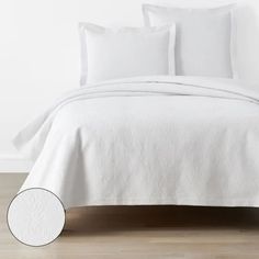 a bed with white sheets and pillows on top of wooden floor next to a wall