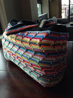 a multicolored crocheted bag sitting on top of a wooden table next to a window