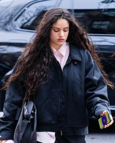 a woman with long hair is walking down the street wearing a black jacket and pink shirt