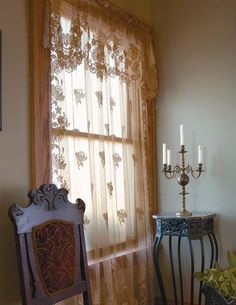 a chair and table in front of a window with sheer curtains on the windowsill