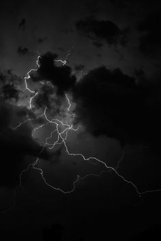 a black and white photo of lightning in the night sky with dark clouds behind it