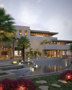 a large modern house is lit up at night with water running through the front yard