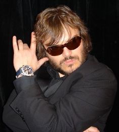 a man in a suit and sunglasses holding his hand up to the side with both hands