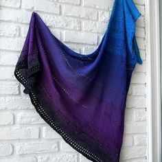 a purple and blue shawl hanging on a white brick wall next to a window