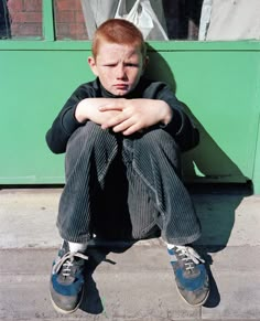 a young man sitting on the sidewalk with his hands folded in front of his face