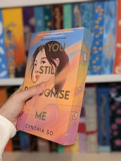 a person holding up a book in front of bookshelves with children's illustrations