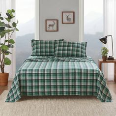 a green and white plaid comforter set on a bed in a room with potted plants