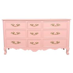 a pink dresser with gold trimmings on the top and bottom drawers, against a white background