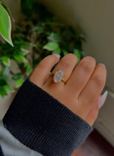 a woman's hand with a ring on it and a plant in the background