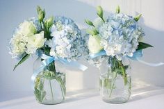 three clear vases with white and blue flowers in them, tied together by a ribbon