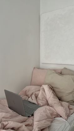 an open laptop computer sitting on top of a bed covered in pink sheets and blankets