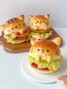 three cat burgers sitting on top of a white plate next to a wooden cutting board