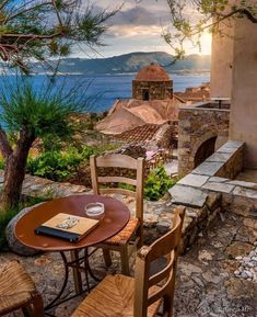 an outdoor table with two chairs and a book on it in front of the ocean