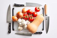 a cutting board with tomatoes, garlic and onions on it next to a large knife