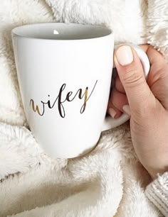 a person holding a coffee mug with the word wife written on it in gold ink