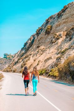 two women are walking down the road with their skateboards in one hand and holding hands