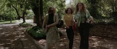 three women are walking down the sidewalk in an area with trees and stone walkways