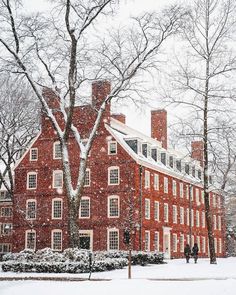 a large red brick building surrounded by trees covered in snow with people walking on the sidewalk