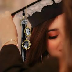 a woman wearing a graduation cap and gown holding a tassel with two pictures hanging from it