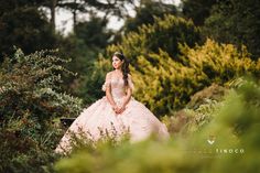 a woman in a pink dress is posing for a photo outside with bushes and trees behind her