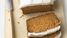 three slices of carrot cake with frosting on a cutting board next to a knife