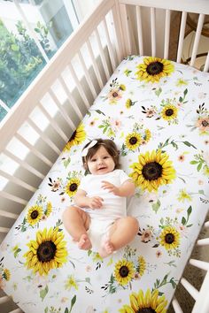 a baby sitting in a crib with sunflowers on it