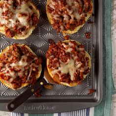 four mini pizzas with meat and cheese on a baking tray next to a knife