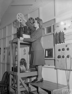 a woman standing on top of a wooden shelf holding a movie projector in her hand