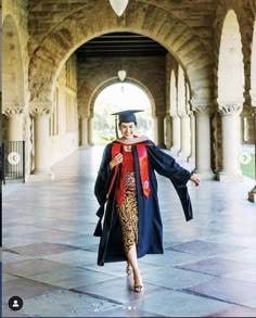 a woman in a graduation gown and cap walks through an archway