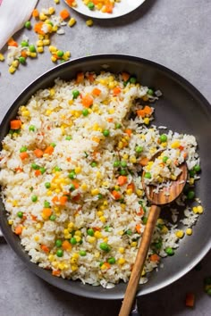 rice with peas and carrots in a skillet next to a wooden spatula