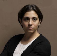 a woman with her arms crossed looking at the camera and posing for a photo in front of a brown wall