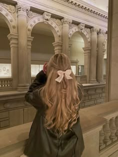 a girl with long hair and a bow in her hair looking at herself in the mirror