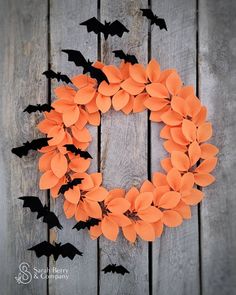 a wreath made out of orange paper with bats hanging from it on a wooden fence