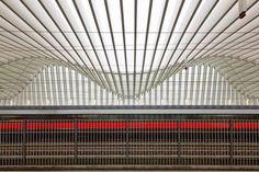 a red train traveling through a train station next to a tall metal structure with bars on it