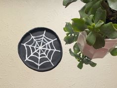 a spider web painted on a black plate next to a potted plant with green leaves