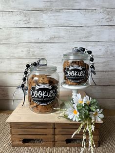 two jars filled with cookies sitting on top of a wooden box next to a flower