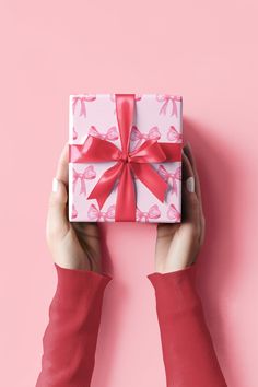 a woman's hands holding up a pink and white present box with red ribbon