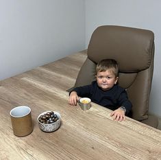 a little boy sitting at a table with some food in front of him and two cups on the table