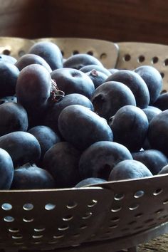 a metal bowl filled with blueberries on top of a wooden table