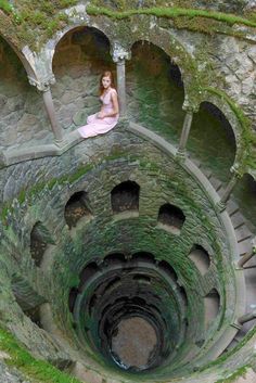 a woman sitting on the top of a spiral staircase in a stone building with moss growing all over it