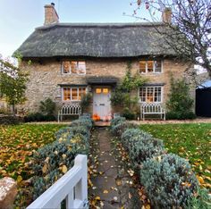 an old stone house with a thatched roof and white picket fence in the front yard