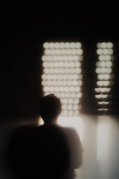 a blurry image of a person standing in front of two windows with blinds on them