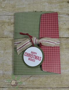 a christmas card with a tag on it and some ribbon tied around the edge, sitting on top of a piece of wood